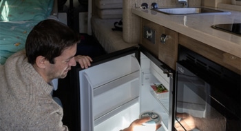 Person placing food inside a built-in camper refrigerator in a compact camper van kitchen.