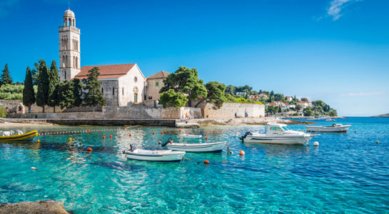 Clear blue water with small boats and old church in the background in Croatia