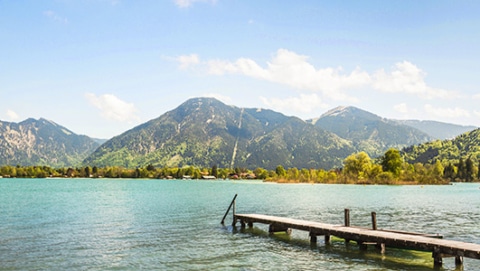 Pier at lake Tegernsee in Germany leading into the lake and mountains visible on the other side of the river.