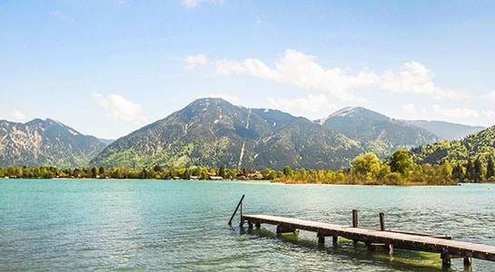 Pier at lake Tegernsee in Germany leading into the lake and mountains visible on the other side of the river.