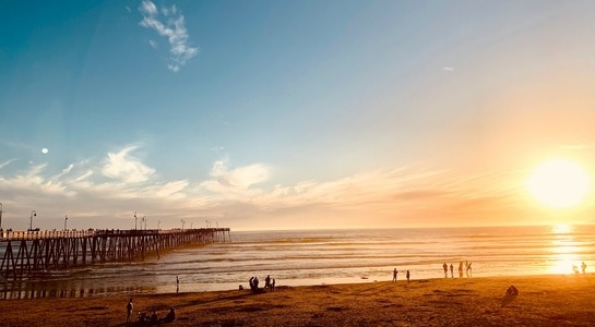 Golden sunset over the pier at Pismo Beach with people enjoying the sand, a lively highlight of Central California beaches.