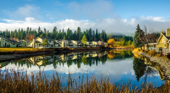 Lakeside homes reflected in still water surrounded by pine forest in Plumas County—an unexpected view along a California road trip through Feather River Canyon.