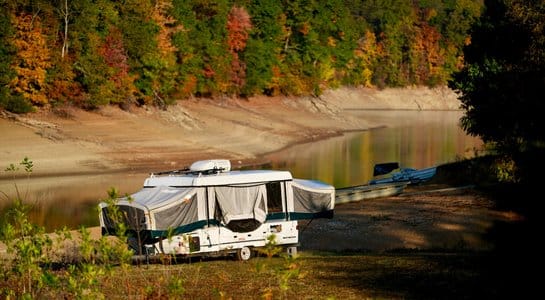 Pop-up camper set up near a calm lake surrounded by autumn trees