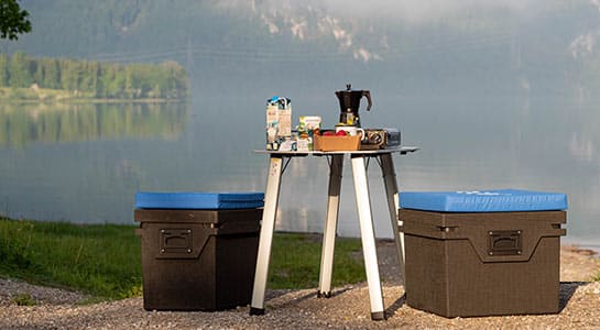 Zwei Qool Kühlboxen als Sitzmöglichkeiten neben einem gedeckten Camping vor einem See