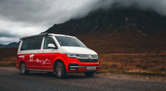 red roadsurfer campervan in front of a mountain covered in clouds
