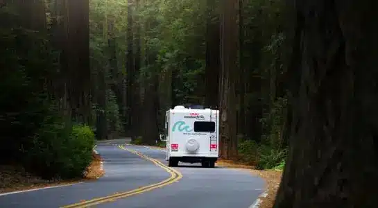 RV driving through the scenic forest roads of Redwood National Park in California surrounded by giant redwoods.