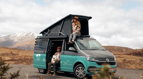 Renting a camper with a pop-top camper van centered in the frame, parked in a scenic mountain landscape