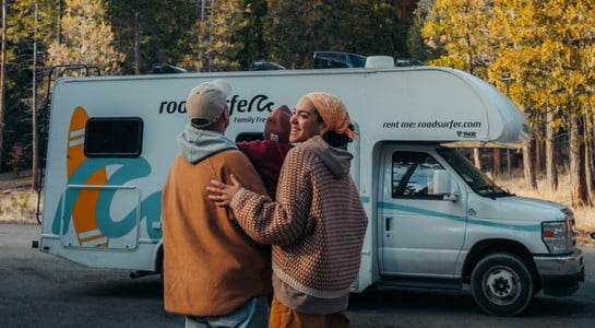 Family standing together in front of a roadsurfer RV rental surrounded by tall trees in a forest