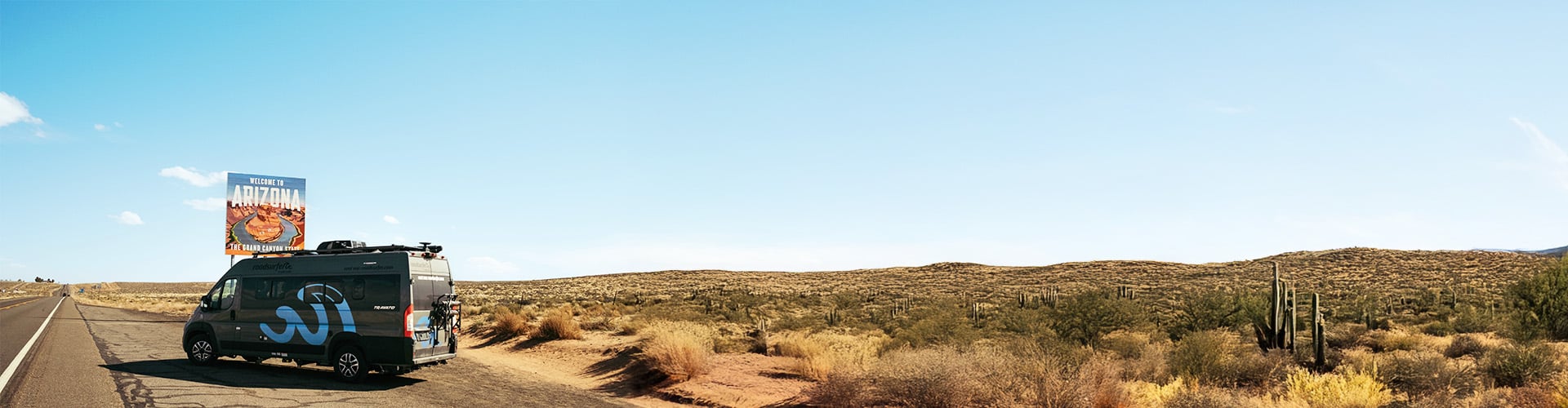 Grey roadsurfer boxvan photograph standing at the roadside in front of a Arizona state sign during a Arizona road trip itinerary.