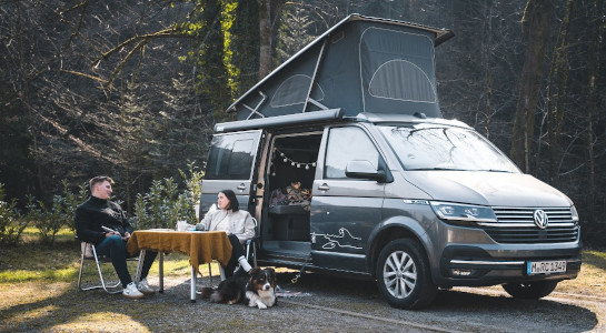 Couple sitting on camping chairs in front of a campervan with a dog