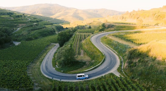 roadsurfer camper driving on a scenic road through vineyards