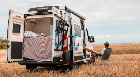 Relaxed man sitting next to a campervan on a field in summer
