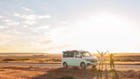 roadsurfer camper van with two happy girls and a dog next to a field in the sunlight