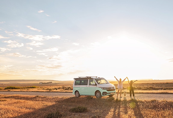 roadsurfer camper van with two happy girls and a dog next to a field in the sunlight