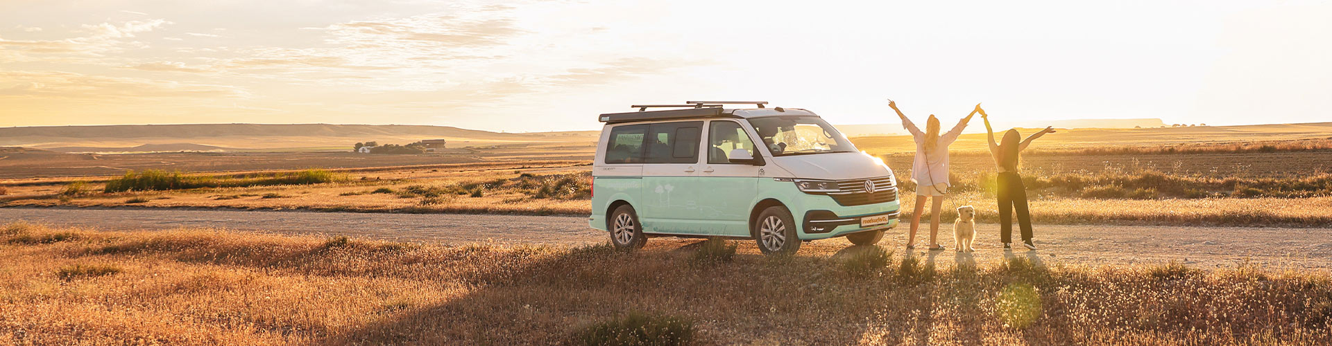 roadsurfer Campervan with two happy girls and a dog next to a field in the sunlight