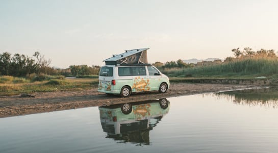 roadsurfer campervan parked by a lake, reflection in the water