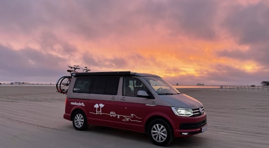 roadsurfer campervan with bike rack parked on a beach, sunset in the background