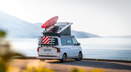 White roadsurfer campervan with kayak parked by a lake