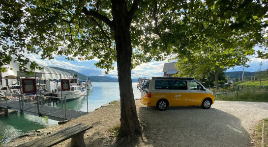 Yellow and white roadsurfer campervan parked by a lake with jetty and boat