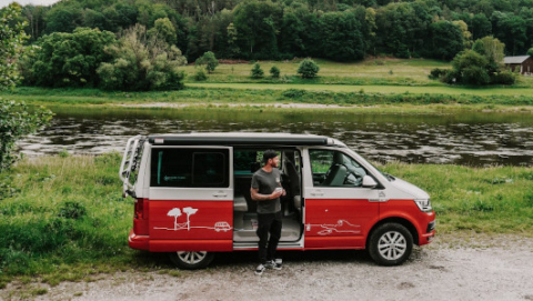 Man standing infront of a camper next to the river