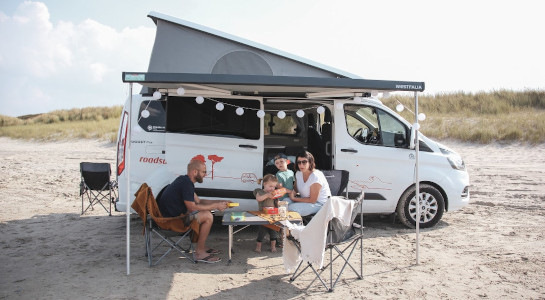 Family sitting at a picnic table in front of a camper at the beach