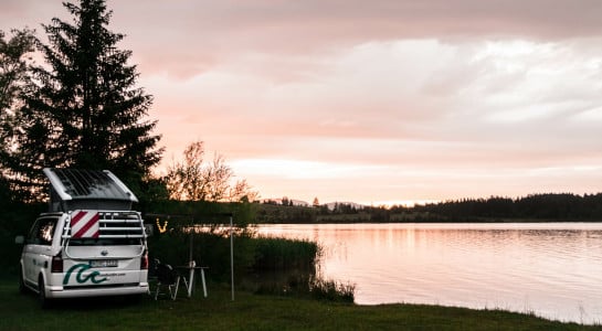 white roadsurfer camper camping by a lake at sunset