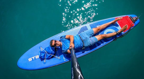 Man dressed in blue lying on a blue SUP in a lake