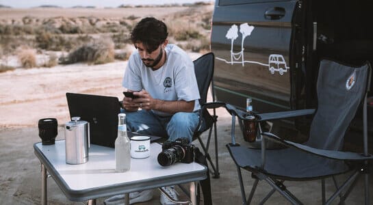 roadsurfer Mitarbeiter beim flexiblen Arbeiten mit seinem Laptop am Campingtisch, draußen neben einem Camper