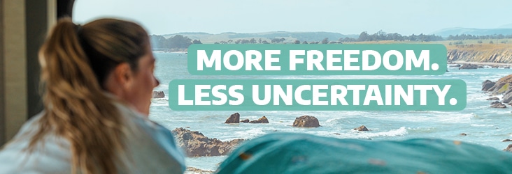 Woman looking out of a camper van towards the sea with the text "more freedom. less uncertainty."