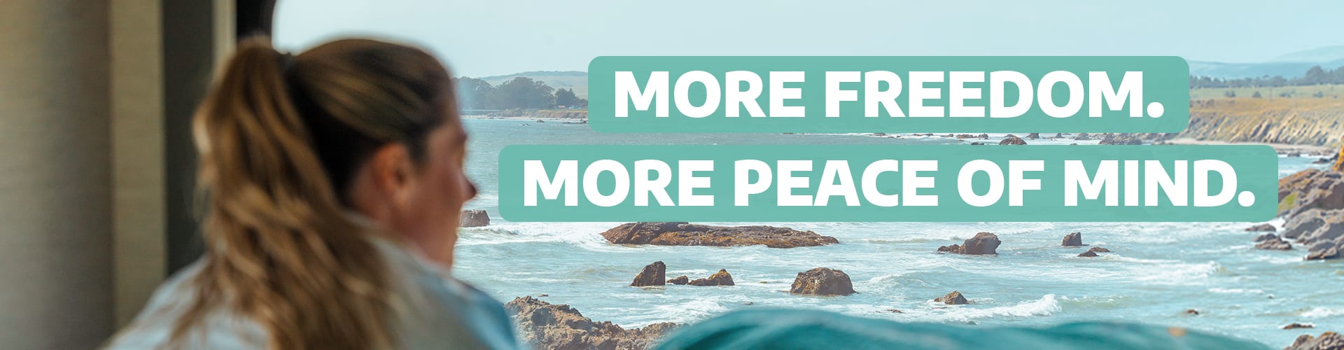 Woman looking out of a camper van towards the sea with the text "More freedom. More peace of mind."