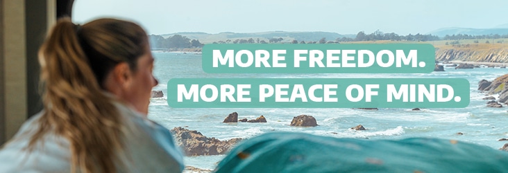 Woman looking out of a camper van towards the sea with the text "More freedom. More peace of mind."