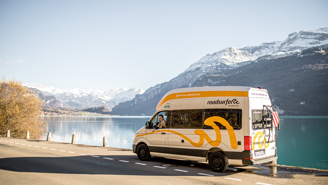 white and yellow camper on a street by a lake, mountains in the background