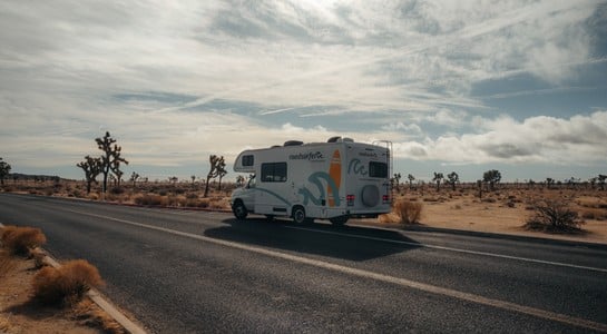 A roadsurfer RV on a desert highway surrounded by Joshua trees under a cloudy sky in Nevada