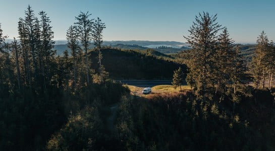 A roadsurfer RV parked in a clearing surrounded by tall evergreen trees and rolling hills in Washington