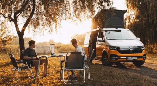 Two men sitting at a picknick table infront of a camper in the sunrise