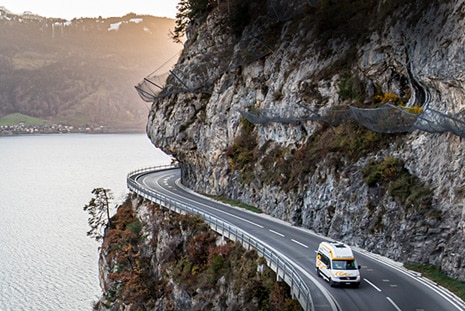 roadsurfer sprinter campervan driving along a rocky mountain road high above a lake