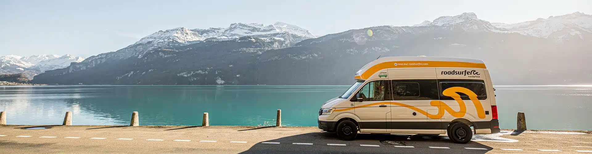 Roadsurfer sprinter van camper in front of a lake and snow-covered mountains in Switzerland