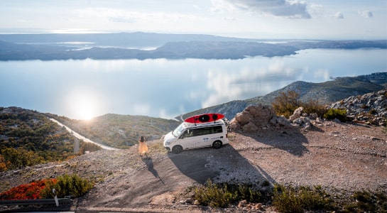 Woman with dress standing next to a camper at a beautiful viewpoint
