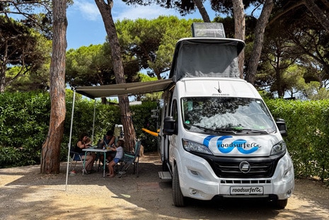 A roadsurfer campervan standing at a campsite with a family having lunch under the awning