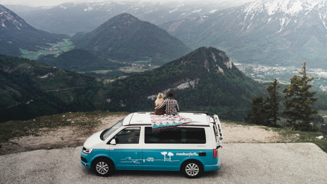 couple sitting on a blanket on their campervan looking at the mountain panorama