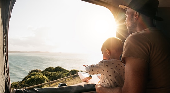 A family with dad and child are sitting in the roof of a campervan looking through the window into the sea