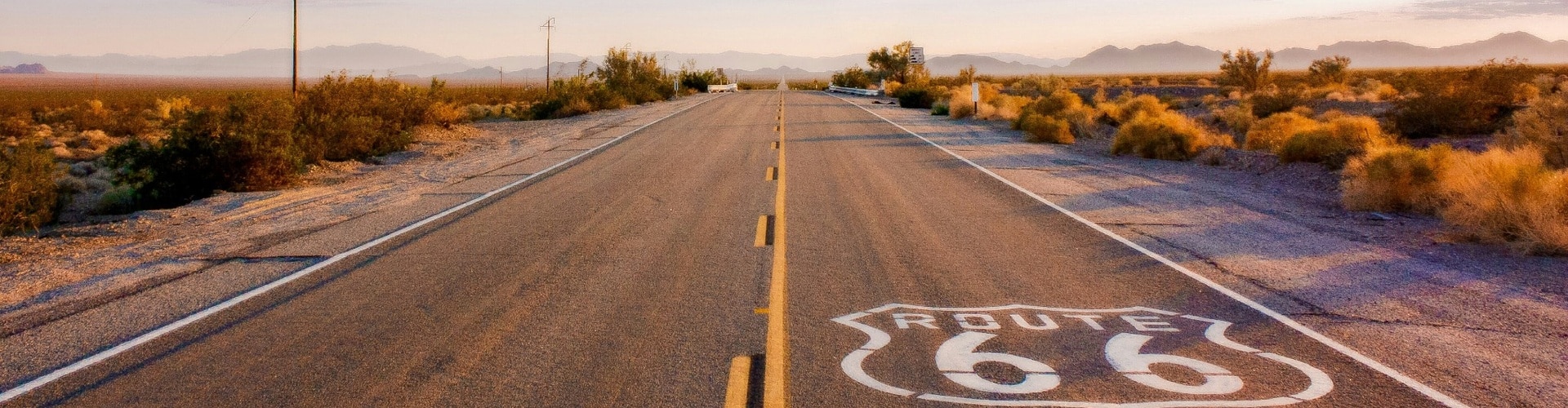Route 66 road trip along a desert highway with the Route 66 shield painted on the pavement at sunset