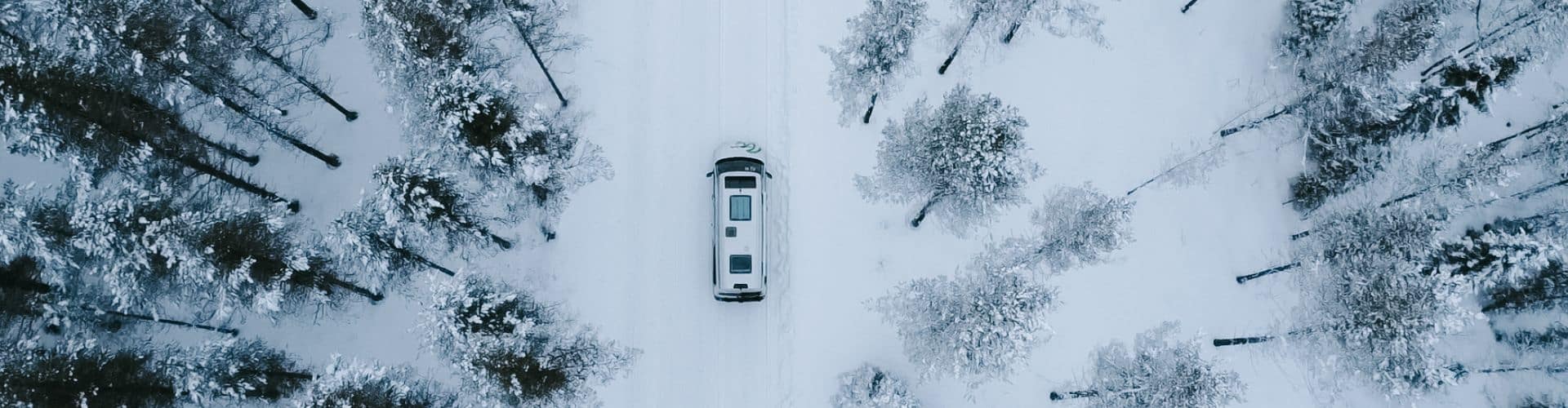 Aerial view of an RV driving on a snow-covered road through a winter forest