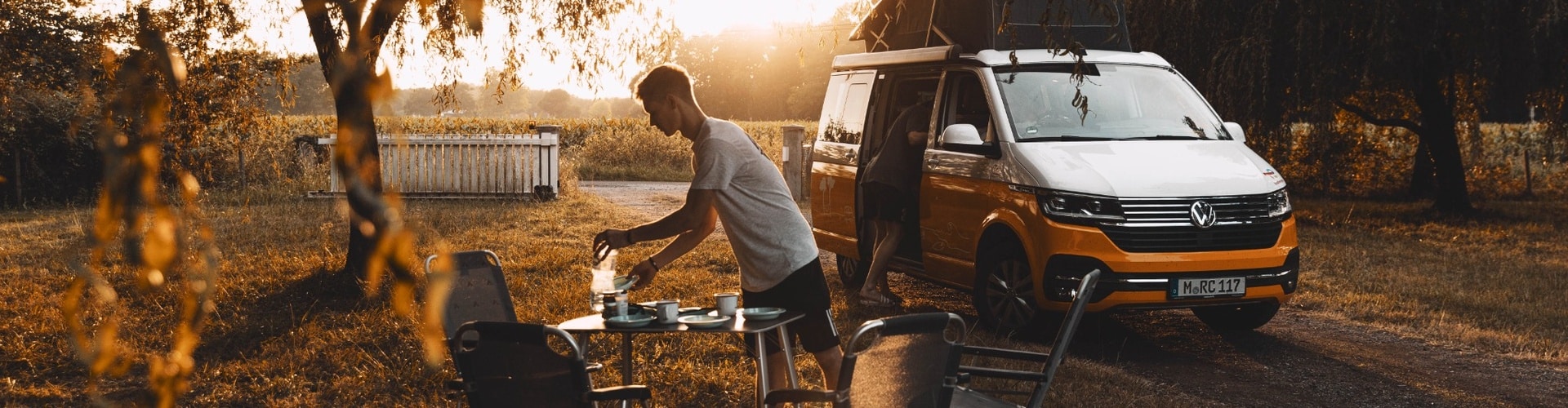 RV camping scene with a camper van parked at a campsite during sunrise, outdoor breakfast table set up beside the van