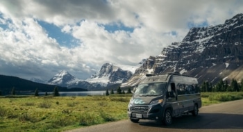 RV parked along a scenic mountain road with snowy peaks in the background, representing the different RV classes.