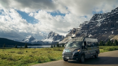 RV parked along a scenic mountain road with snowy peaks in the background, representing the different RV classes.