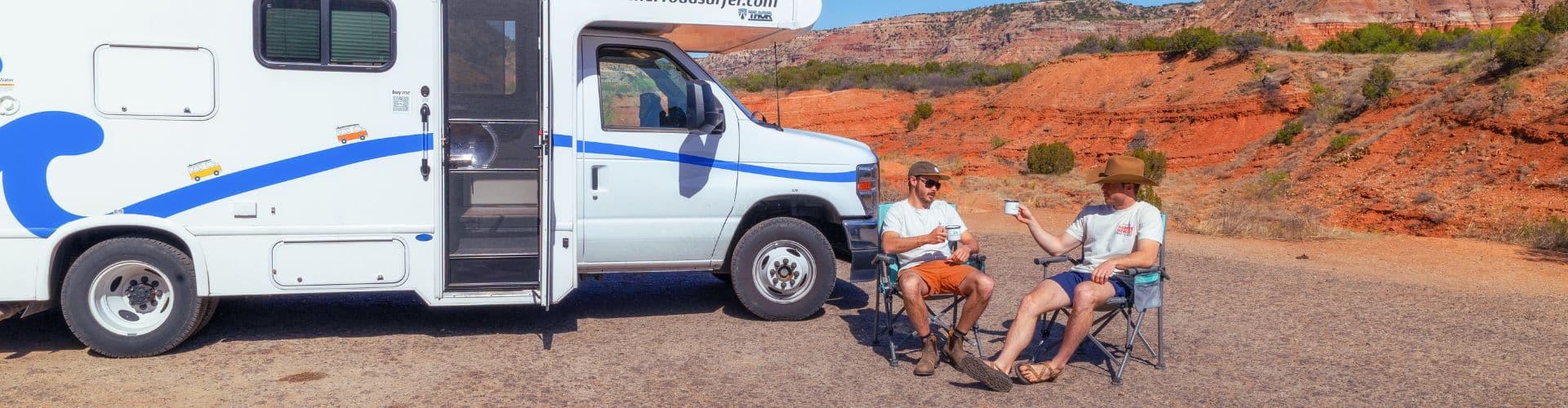 Two travelers sitting in folding chairs beside an RV and chatting in a sunny desert landscape