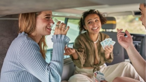 Three people sitting inside an RV playing cards together during a relaxed travel moment