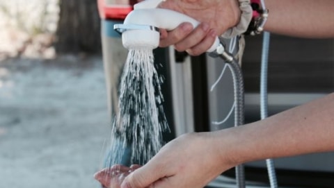 Person testing water flow from an RV's outdoor shower hose held over their hand