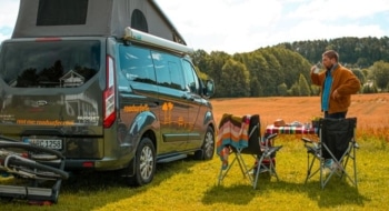 A camper set up at an RV park with chairs and a picnic table in an open field, showing a relaxed outdoor scene perfect for road trips.